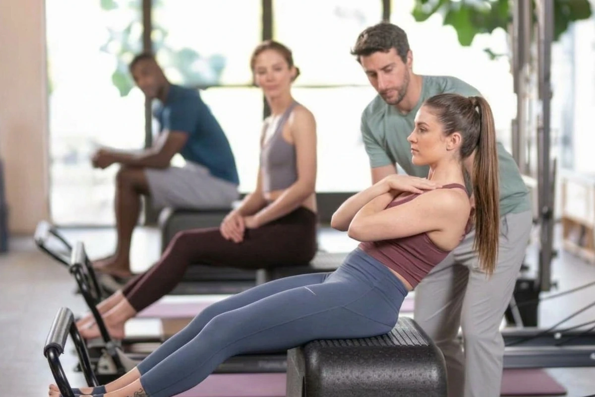Instructor de Pilates ajustando la ejecución de una alumna en el Reformer